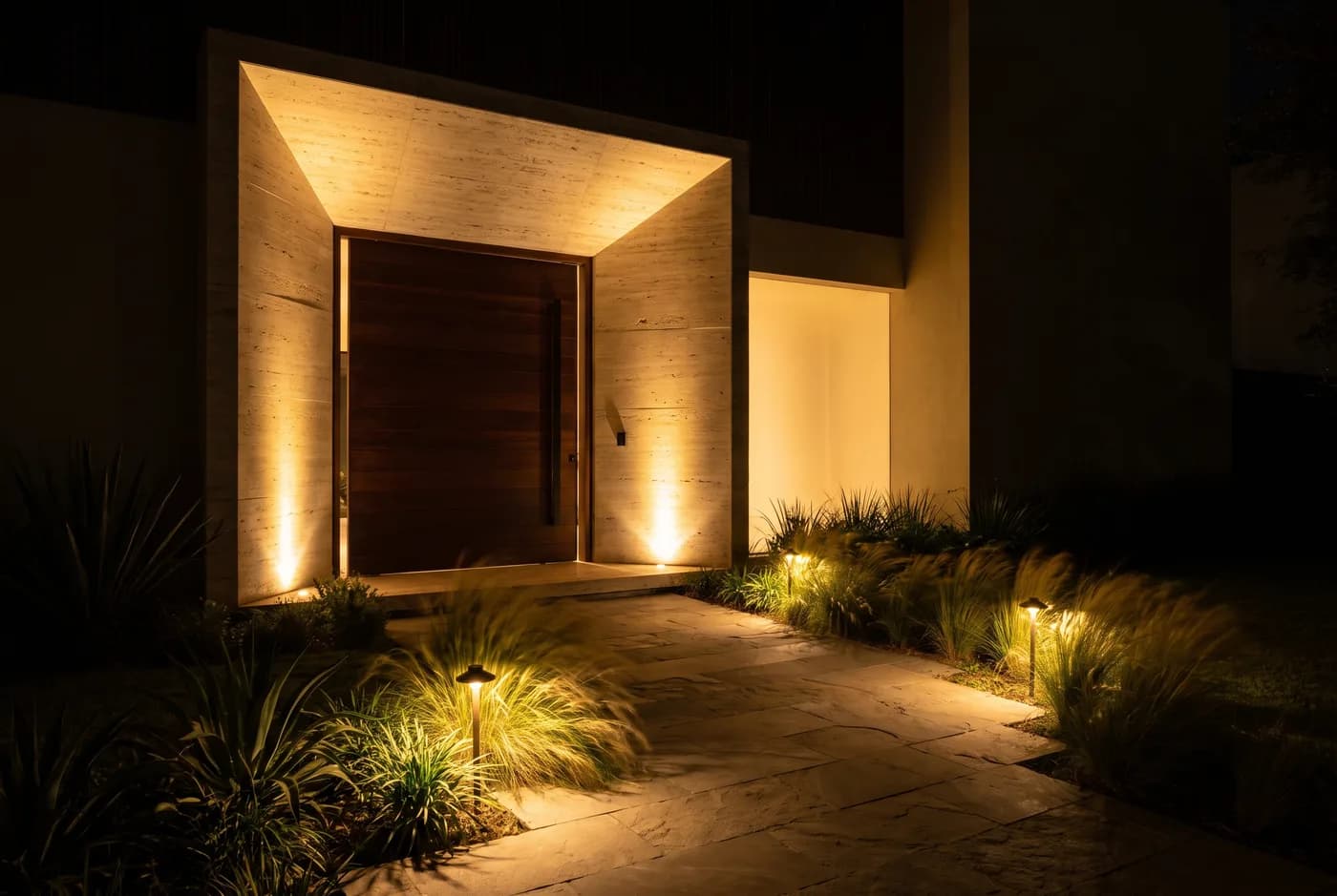 Acesso de uma casa à noite, com caminho balizado por luz baixa